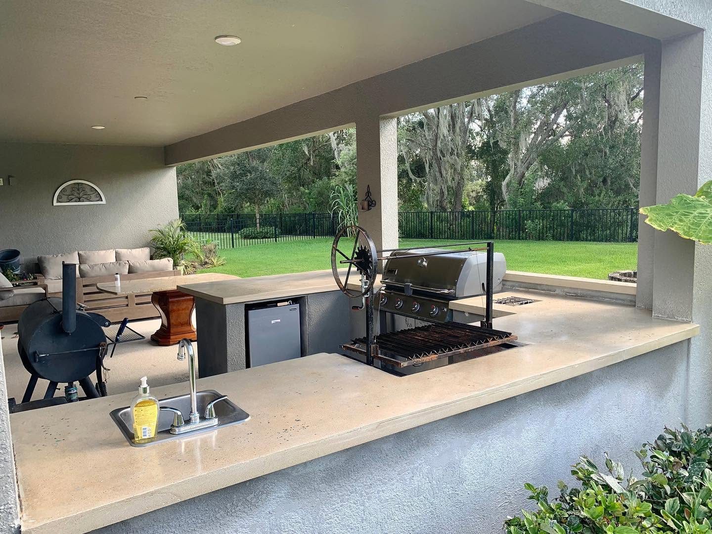 Light concrete countertop on a covered outdoor kitchen with a sink, grill and smoker