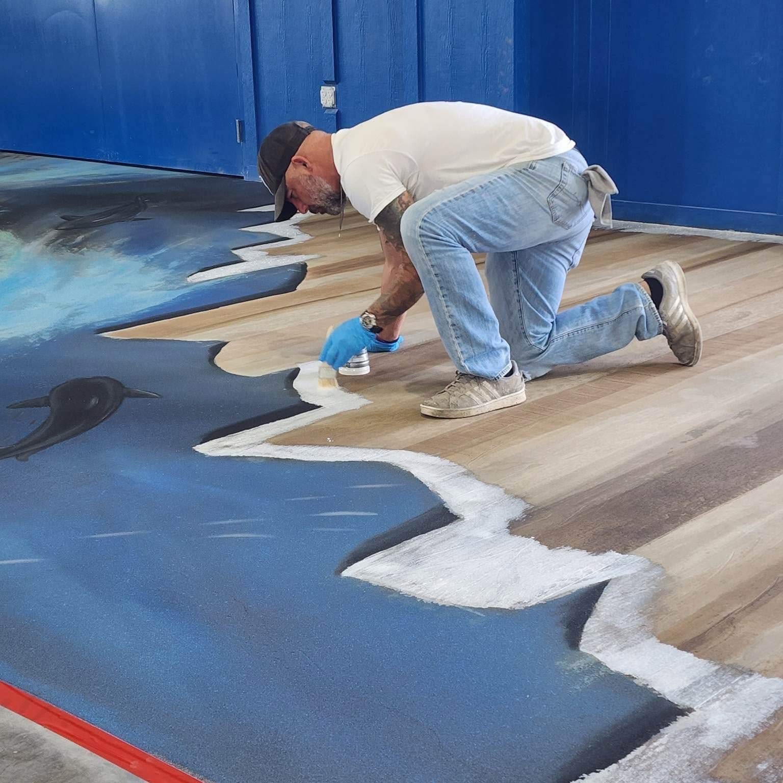 Ben on his knees hand-detailing the shoreline edge of a blue artistic epoxy floor